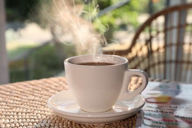 Photo of Cup of delicious coffee on rattan table in morning