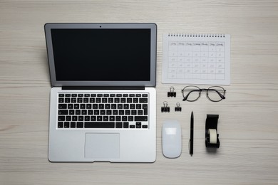 Modern laptop, glasses and office stationery on white wooden table, flat lay. Distance learning