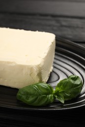 Photo of Block of tasty butter with basil on black wooden table, closeup