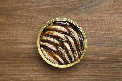 Sprats in tin can on wooden table, top view