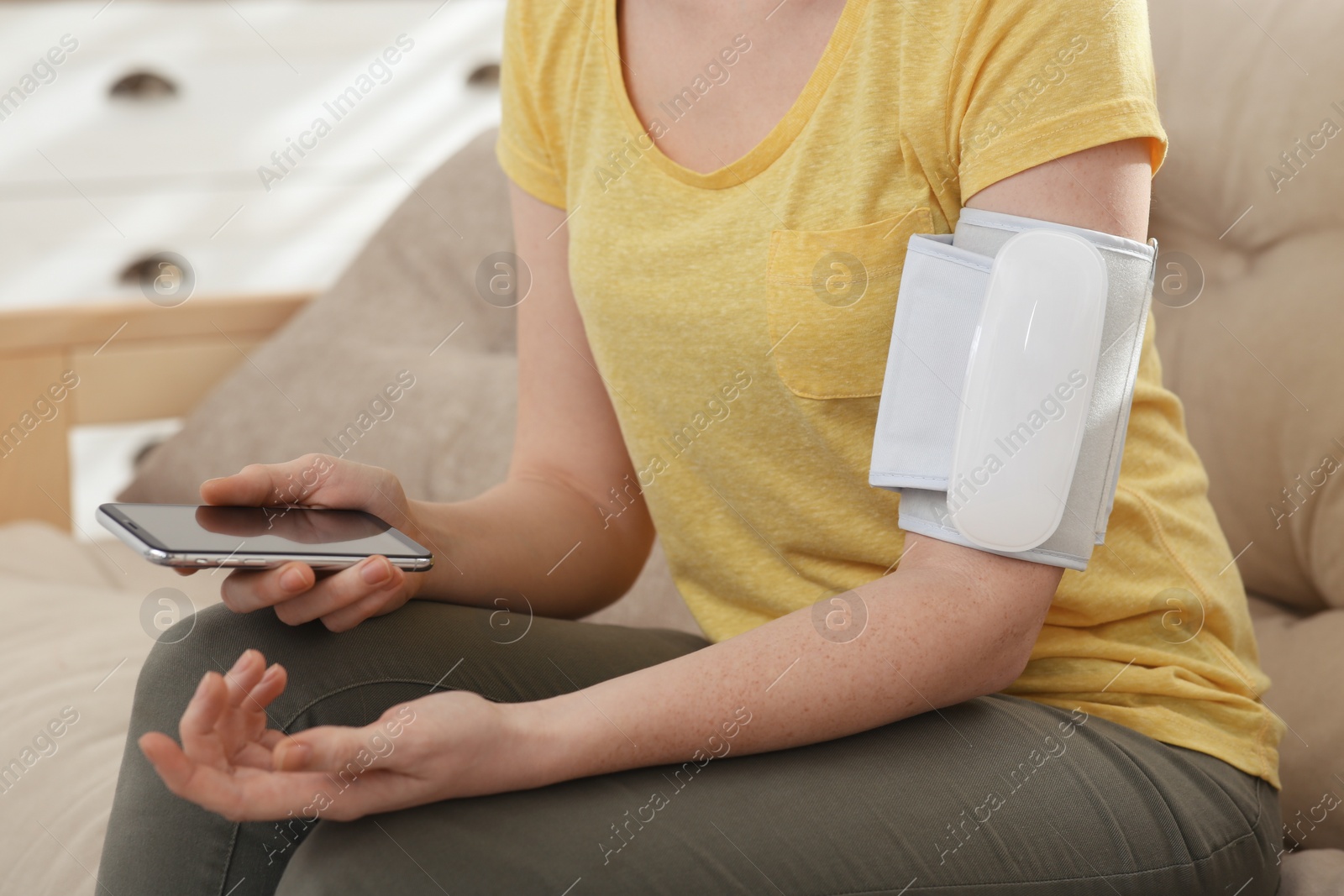 Photo of Woman checking blood pressure with modern monitor and smartphone indoors, closeup