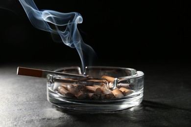 Photo of Smoldering cigarette in ashtray on grey table against black background