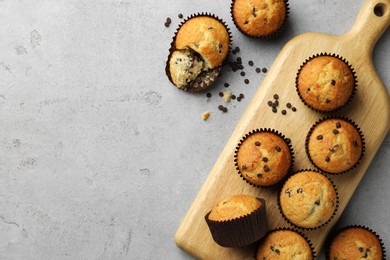 Photo of Delicious sweet muffins with chocolate chips on grey textured table, flat lay. Space for text