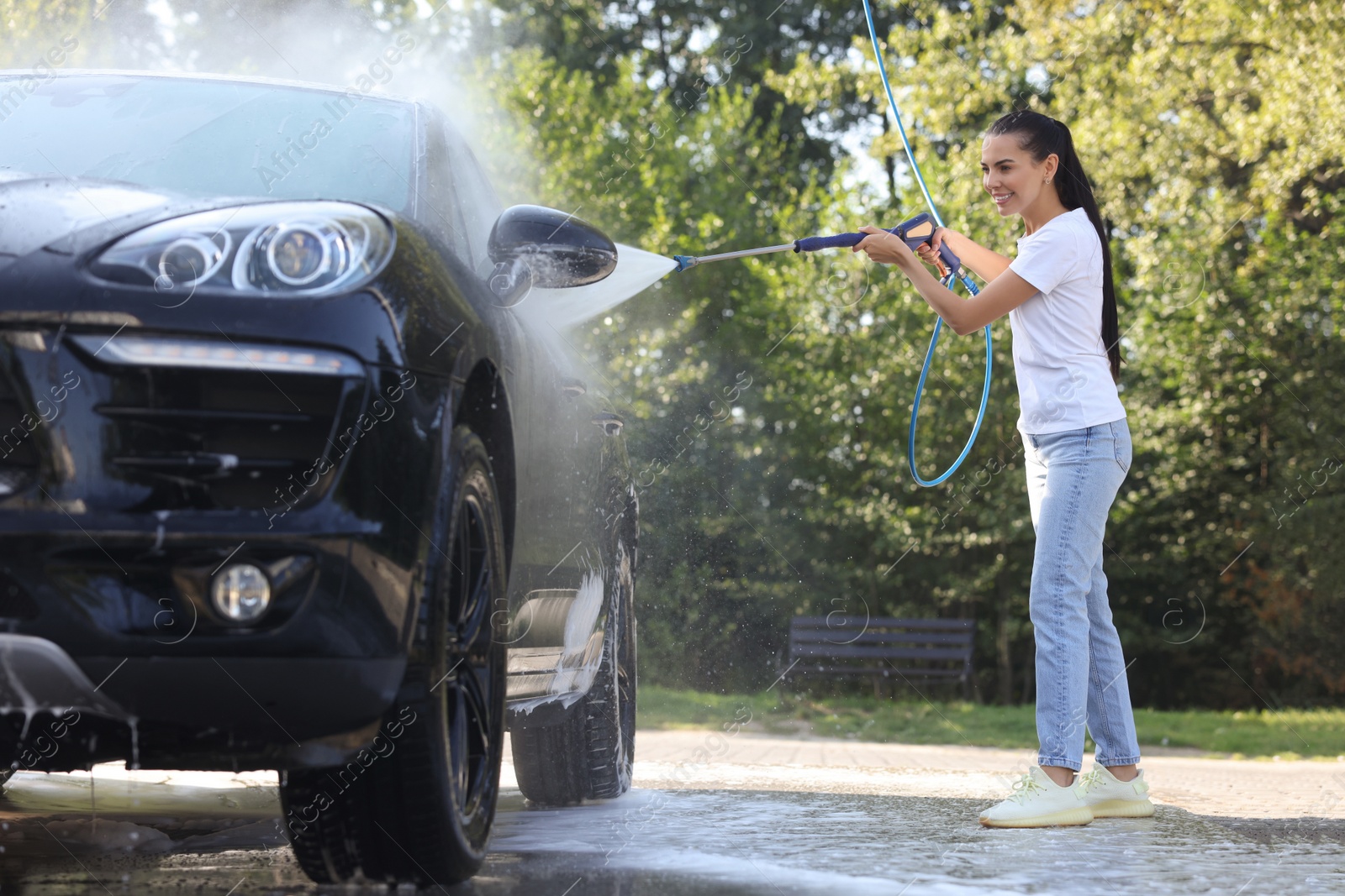 Photo of Happy woman washing car with high pressure water jet outdoors