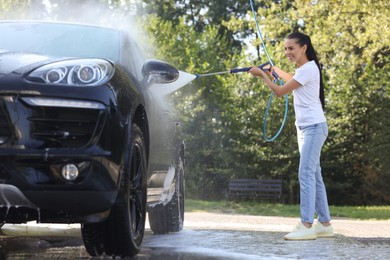 Happy woman washing car with high pressure water jet outdoors