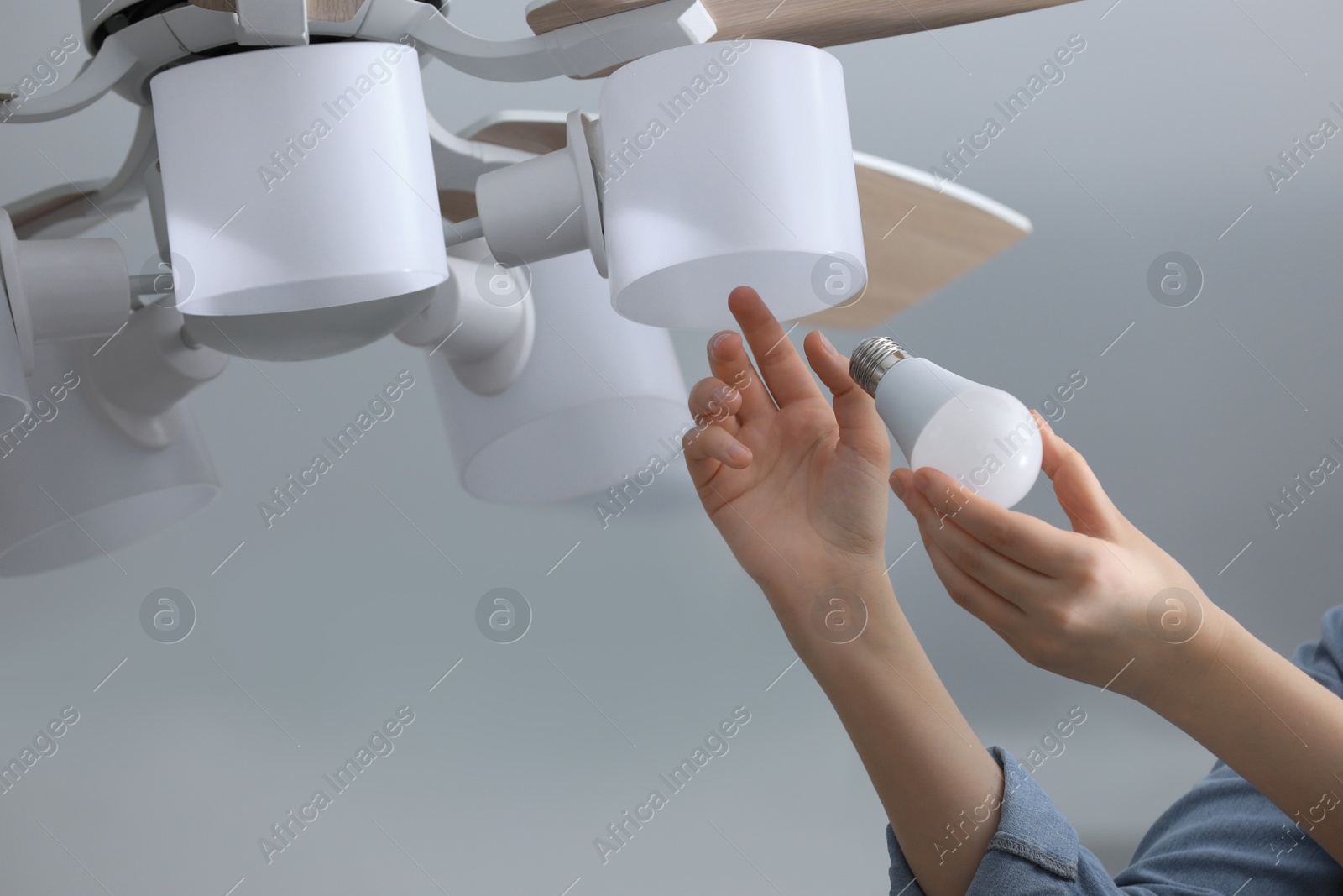 Photo of Woman changing fluorescent light bulb in ceiling lamp at home, closeup. Saving energy concept