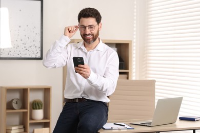 Photo of Portrait of smiling man with smartphone in office