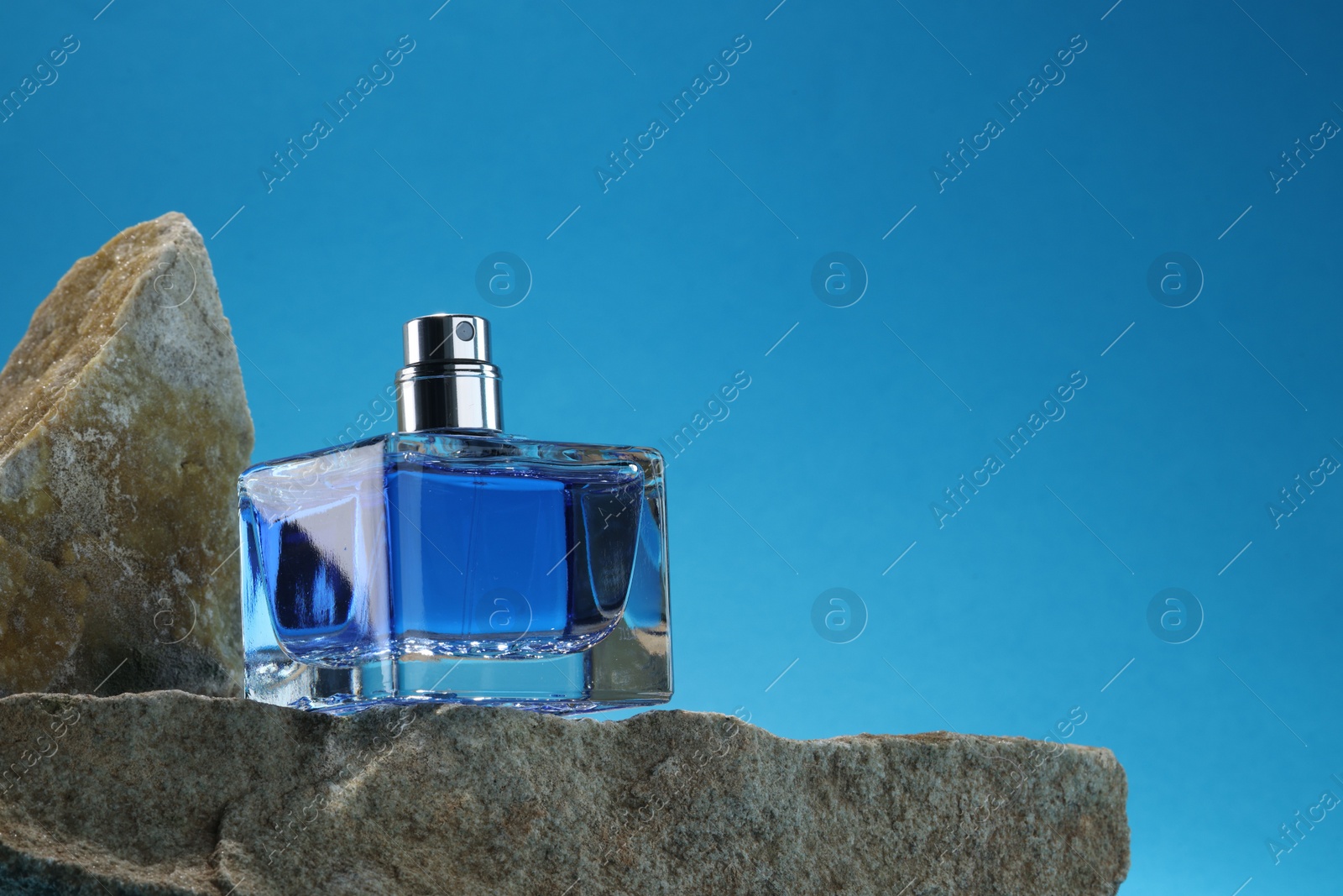 Photo of Stylish presentation of luxury men`s perfume on stones against light blue background. Space for text