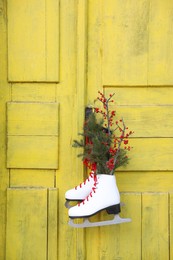 Photo of Pair of ice skates with Christmas decor hanging on old yellow door