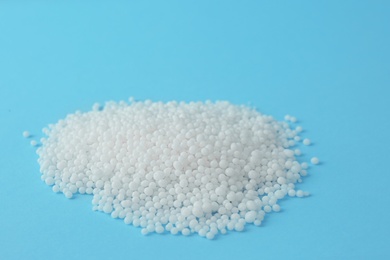 Pellets of ammonium nitrate on light blue background, space for text. Mineral fertilizer