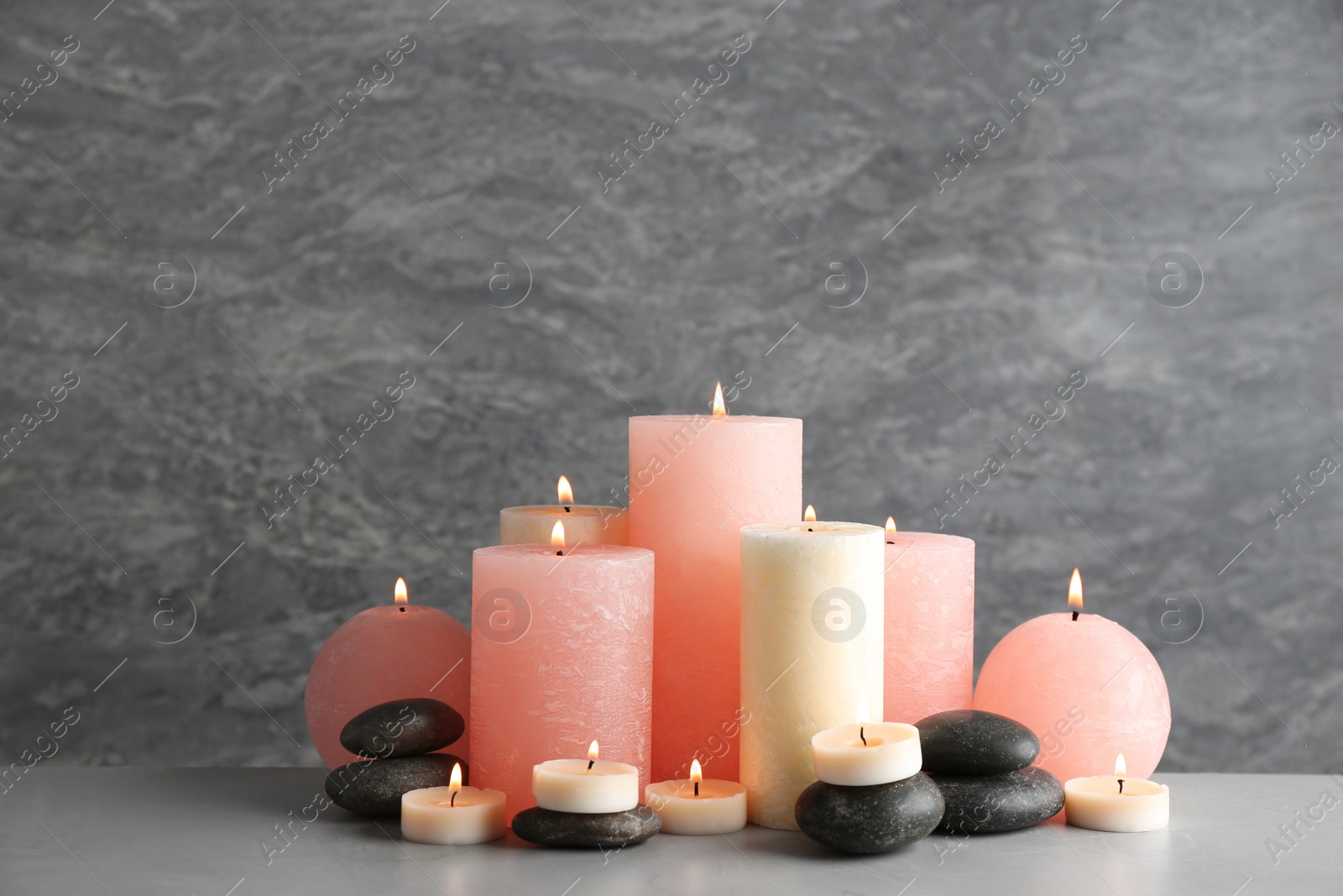 Photo of Beautiful composition with candles and stones on table against grey background. Space for text