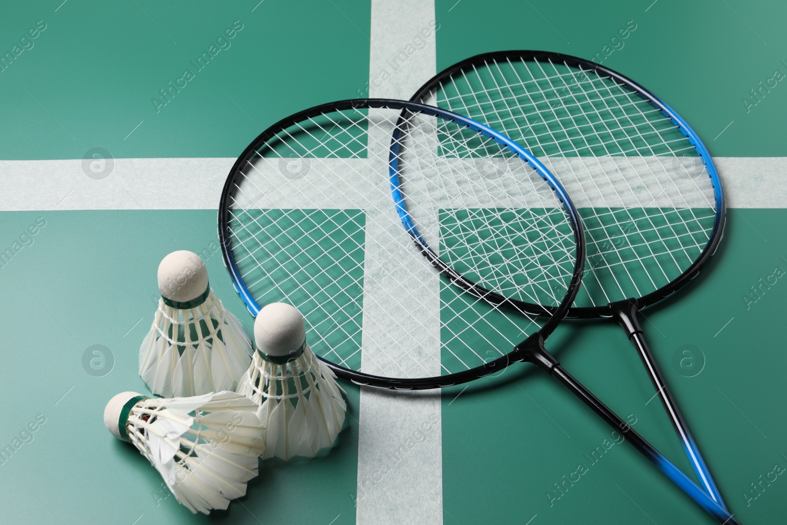 Photo of Feather badminton shuttlecocks and rackets on green table, closeup