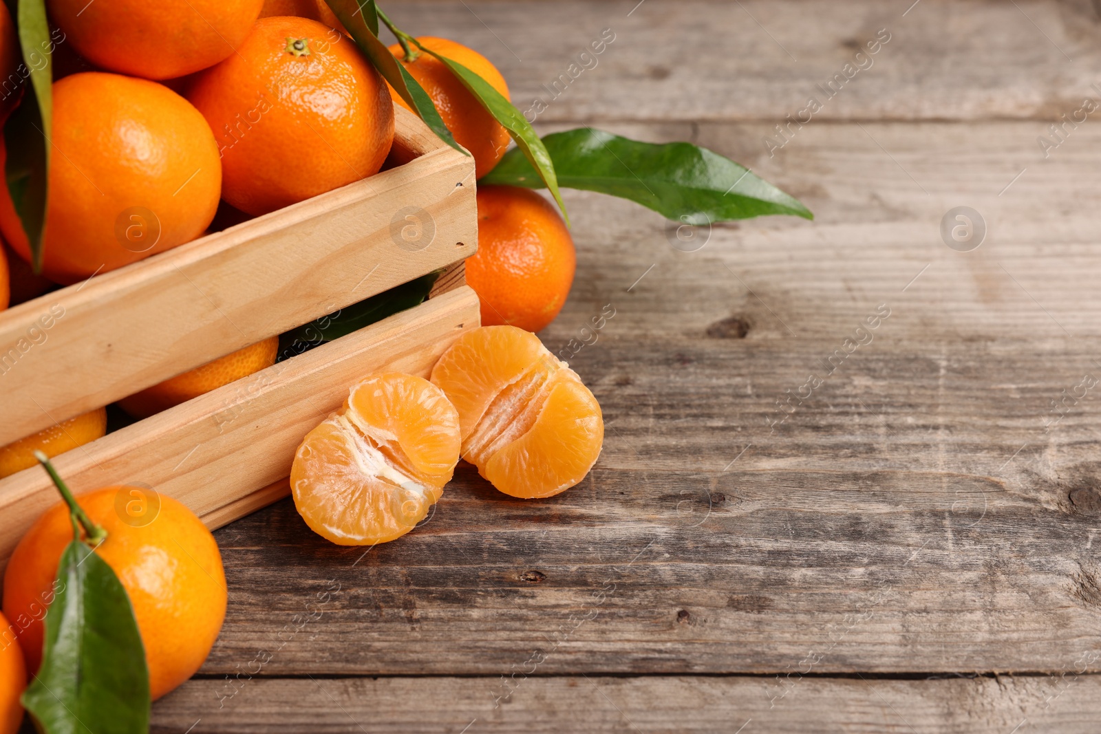 Photo of Delicious tangerines with leaves on wooden table. Space for text