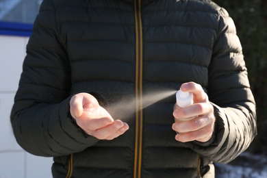 Photo of Man spraying antiseptic onto hand outdoors, closeup