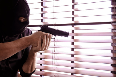 Photo of Man in mask aiming through window blinds indoors