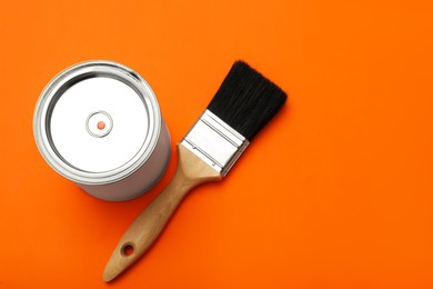 Photo of Can of orange paint and brush on color background, top view. Space for text