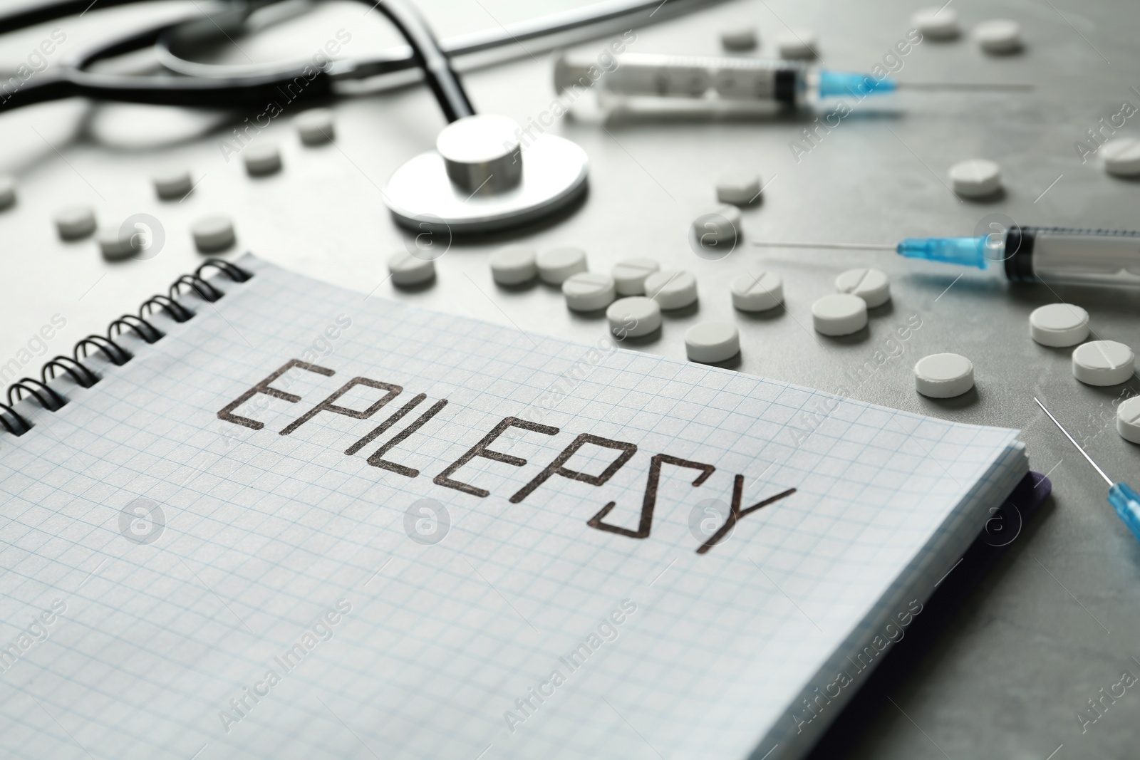 Photo of Notebook with word Epilepsy, pills and syringes on grey table, closeup