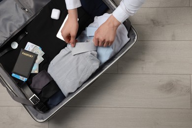 Photo of Man packing suitcase on wooden floor, top view with space for text. Business trip planning