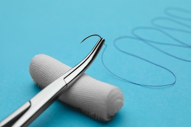 Photo of Forceps with suture thread and bandage roll on light blue background, closeup. Medical equipment