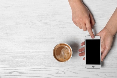 Woman using mobile phone at table with cardboard cup of aromatic coffee, top view