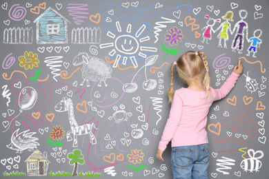 Image of Little girl drawing with colorful chalk on gray wall