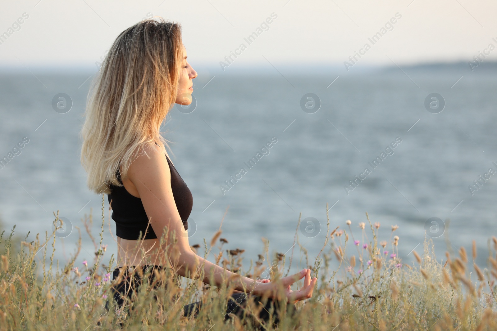 Photo of Young woman meditating near river on sunny day, space for text