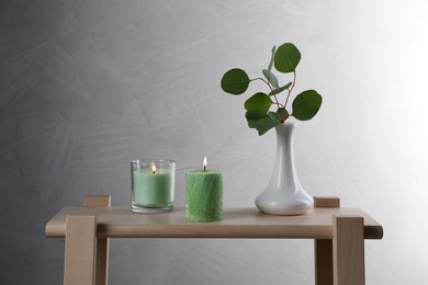 Scented candles near vase with eucalyptus branch on wooden table