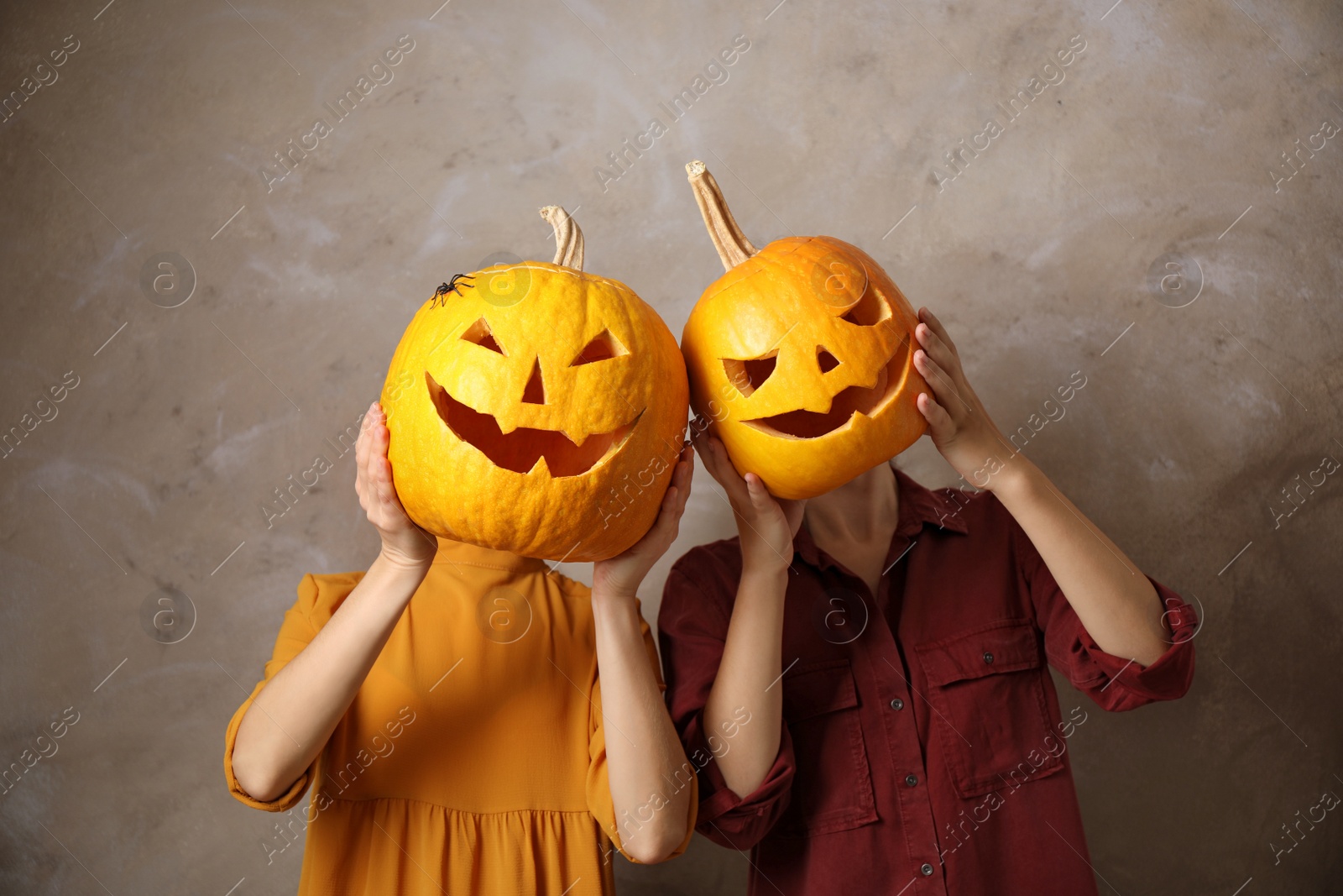 Photo of Women with pumpkin heads against beige background. Jack lantern - traditional Halloween decor