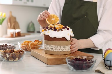Woman decorating traditional Easter cake with dried orange slice at white marble table in kitchen, closeup