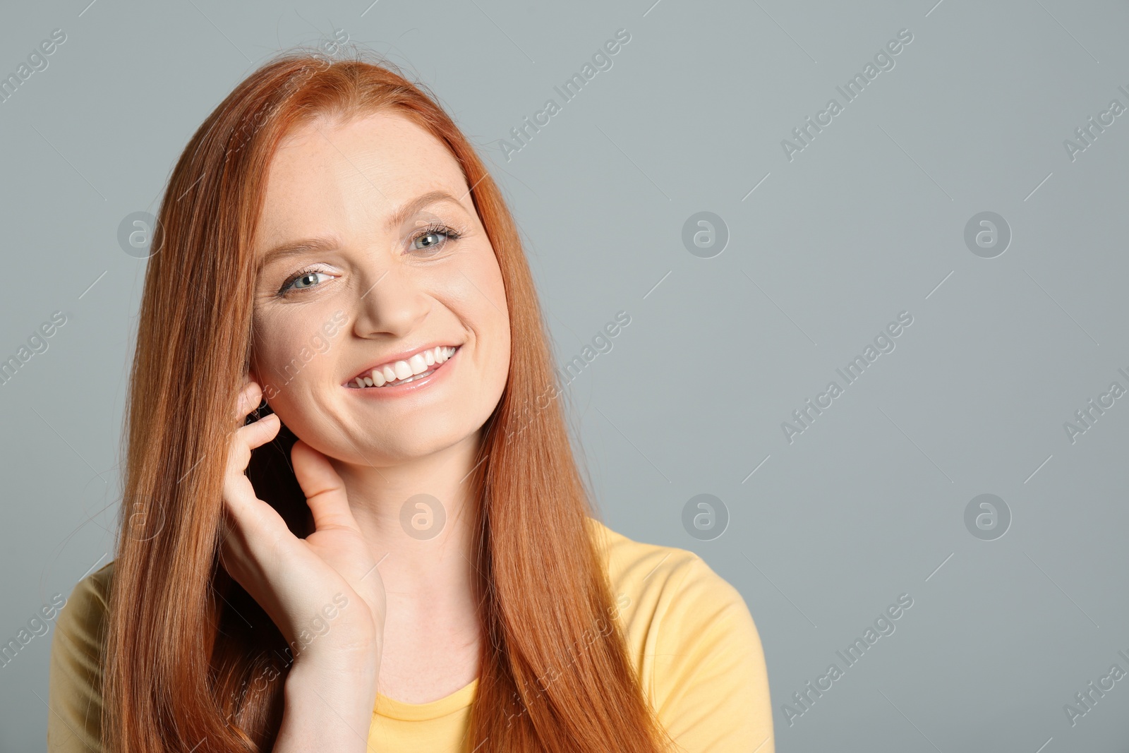 Photo of Candid portrait of happy young woman with charming smile and gorgeous red hair on light grey background, space for text