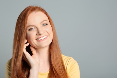 Photo of Candid portrait of happy young woman with charming smile and gorgeous red hair on light grey background, space for text