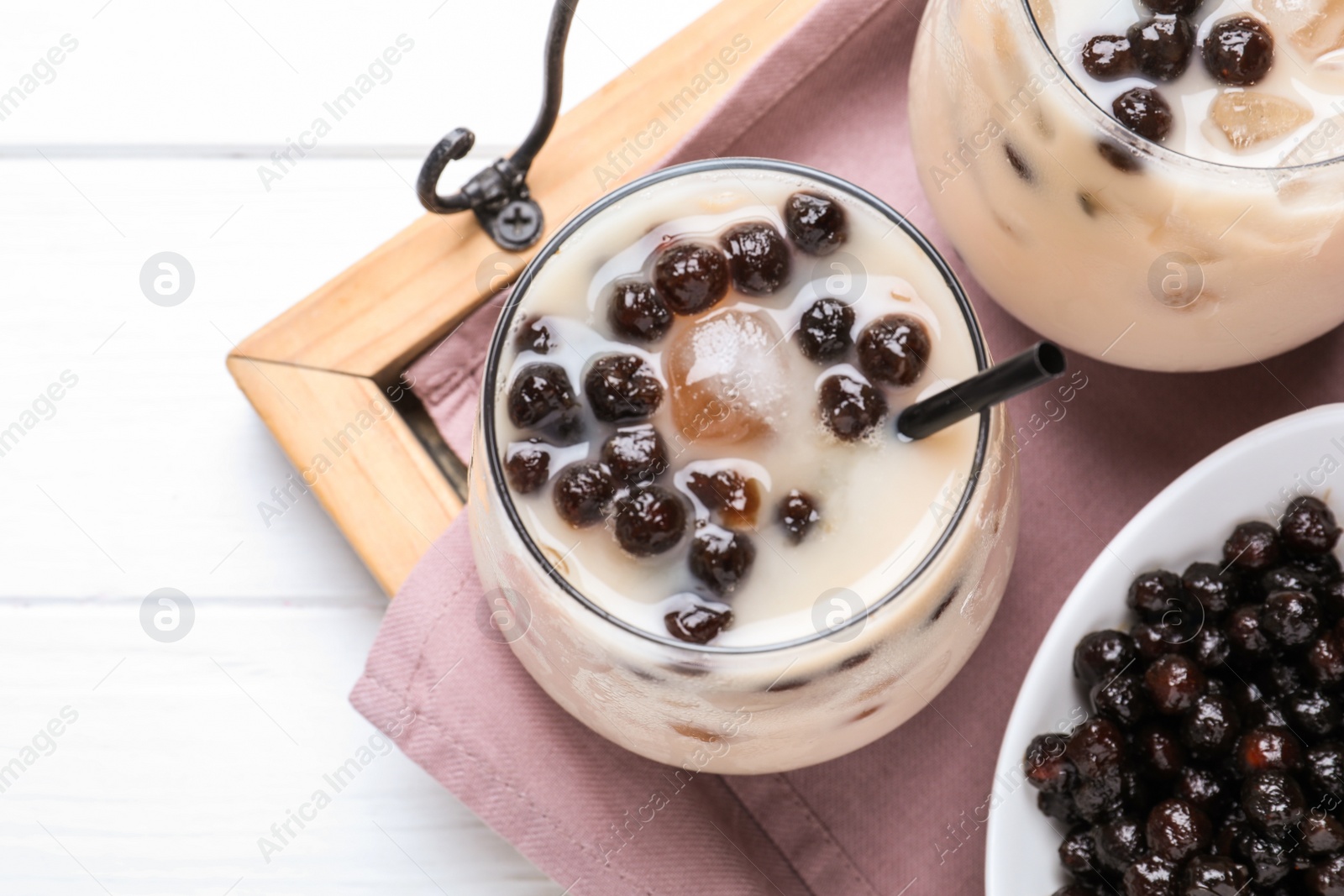 Photo of Bubble milk tea with tapioca balls on white wooden table, top view