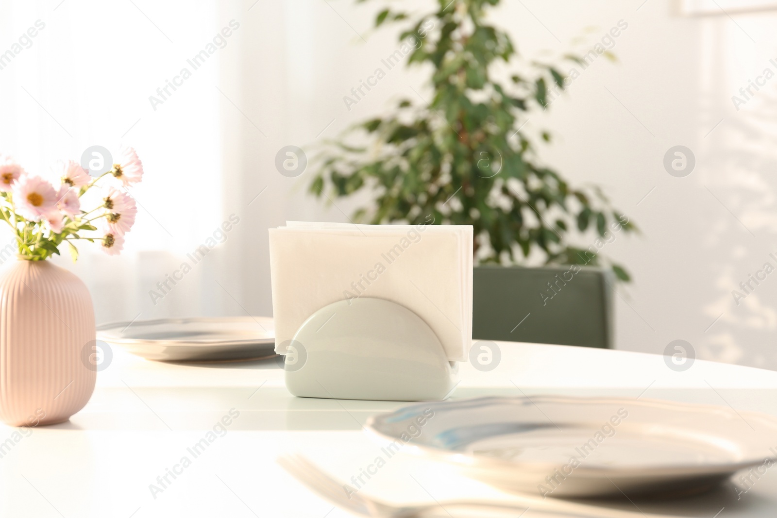 Photo of Ceramic napkin holder with paper serviettes on table indoors