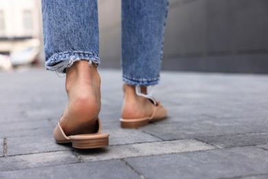 Photo of Woman in blue jeans and fashionable slippers walking on city street, closeup. Space for text