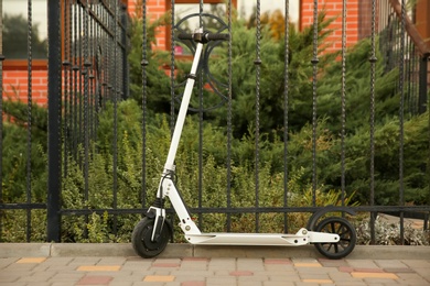 Photo of Modern electric kick scooter near metal fence outdoors