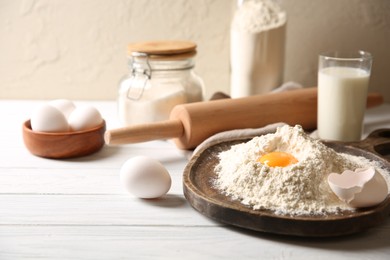 Making dough. Pile of flour with yolk, rolling pin and eggs on white wooden table, closeup