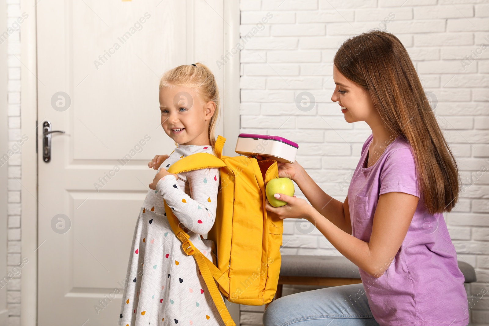 Photo of Young mother putting lunch into her child's school bag at home