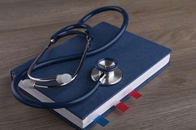Photo of Book with sticker marks and stethoscope on wooden table. Medical education