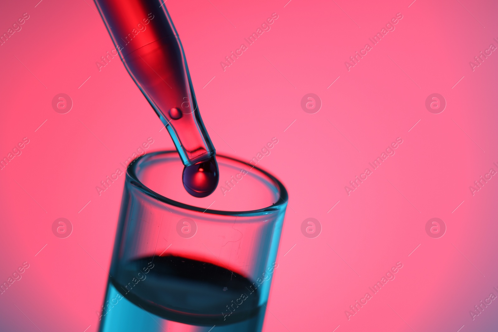 Photo of Dripping liquid from pipette into test tube on color background, closeup. Space for text