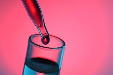 Photo of Dripping liquid from pipette into test tube on color background, closeup. Space for text