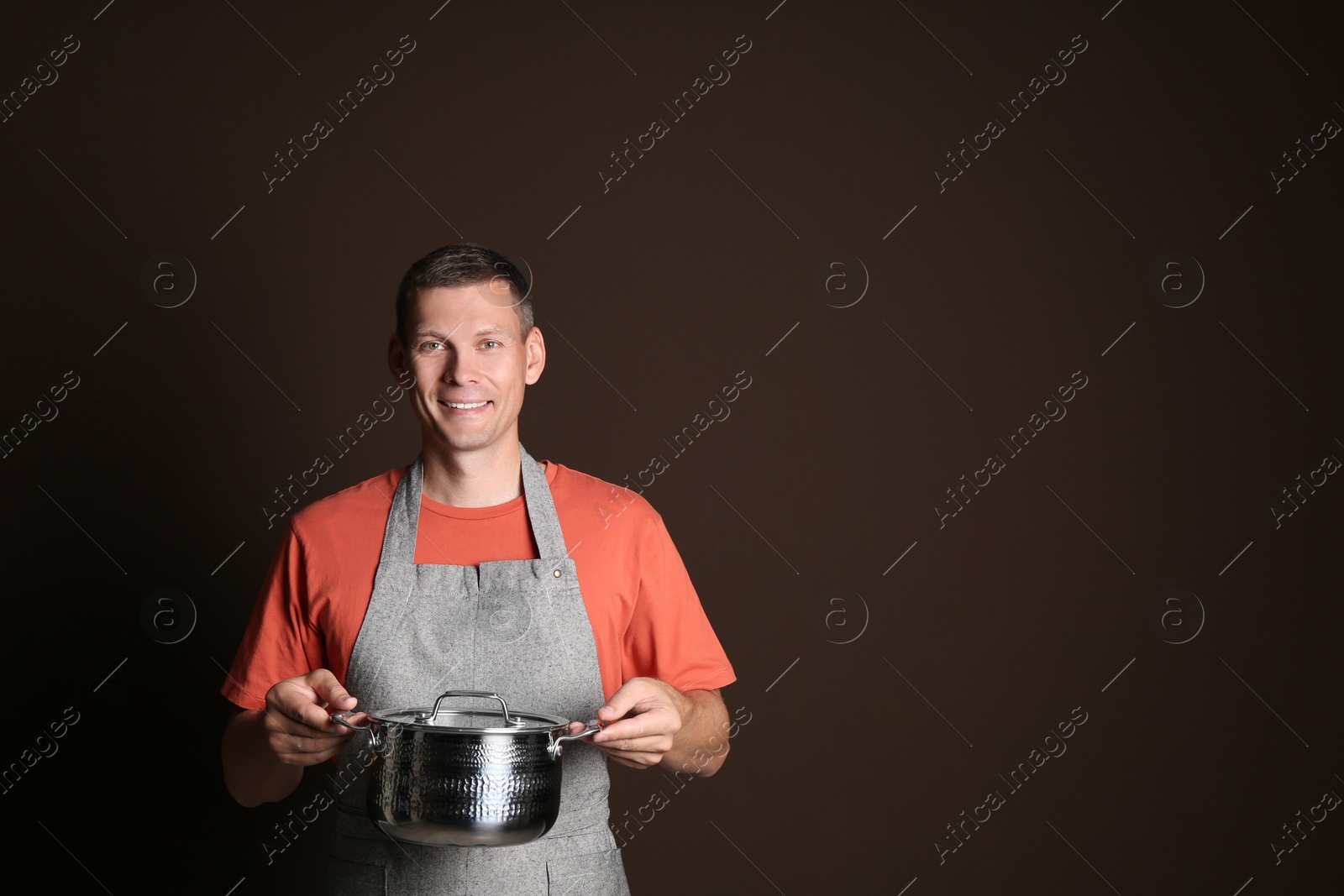 Photo of Happy man with cooking pot on brown background. Space for text