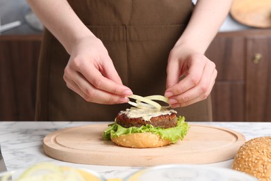 Woman making delicious vegetarian burger at white marble table, closeup