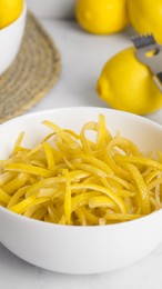 Photo of Bowl with peel pieces, fresh lemons and zester on white marble table, closeup