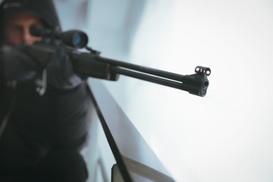 Photo of Hired professional killer indoors, focus on sniper rifle