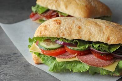 Photo of Delicious sandwiches with fresh vegetables and salami on grey table, closeup