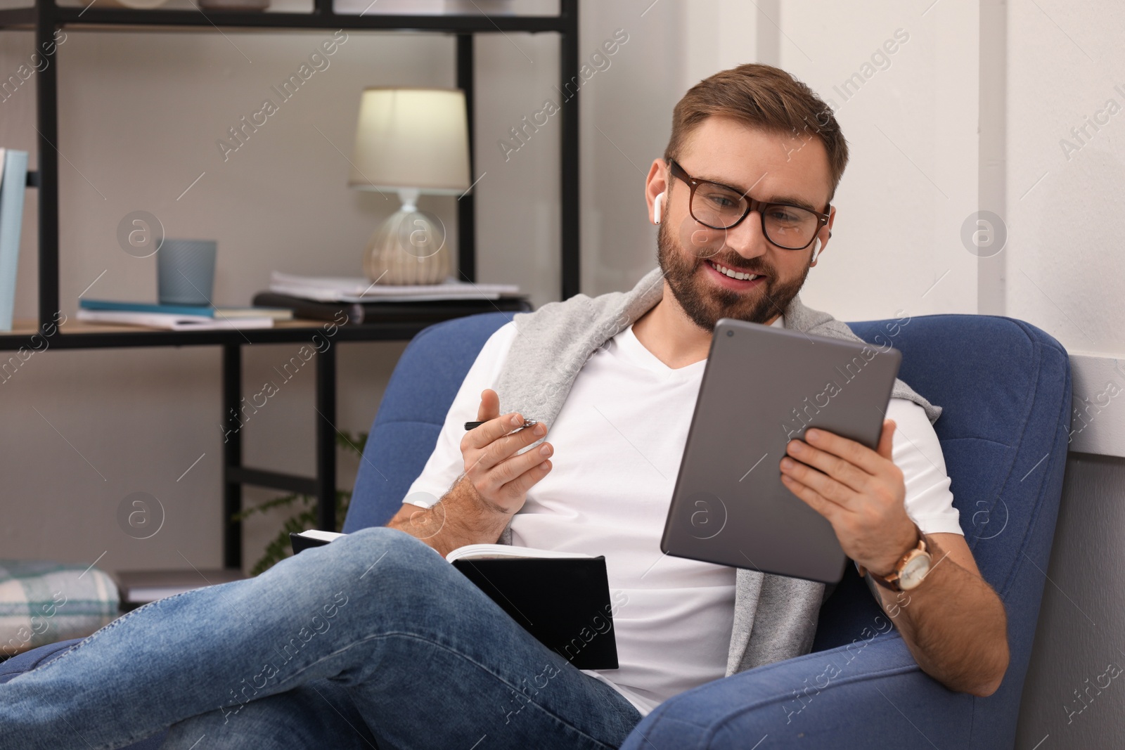 Photo of Young man with earphones working on tablet at home