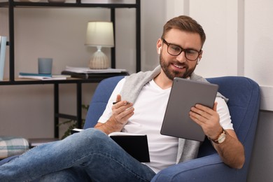 Photo of Young man with earphones working on tablet at home