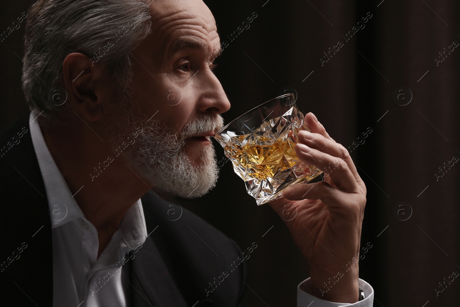 Photo of Senior man in suit drinking whiskey on black background