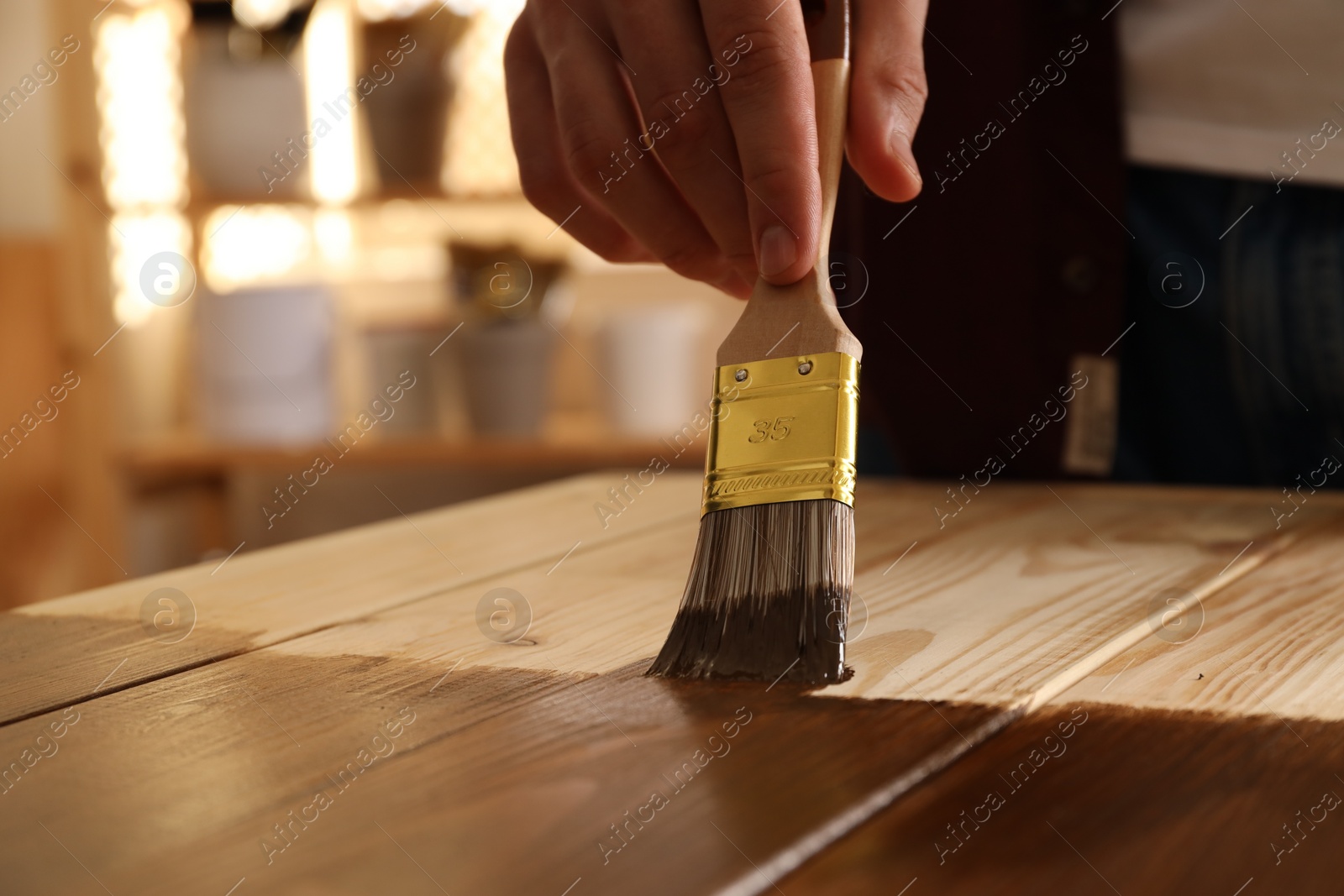 Photo of Man with brush applying wood stain onto wooden surface indoors, closeup