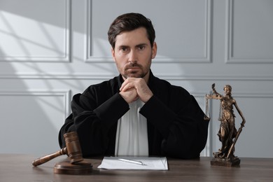 Judge with gavel and papers sitting at wooden table indoors